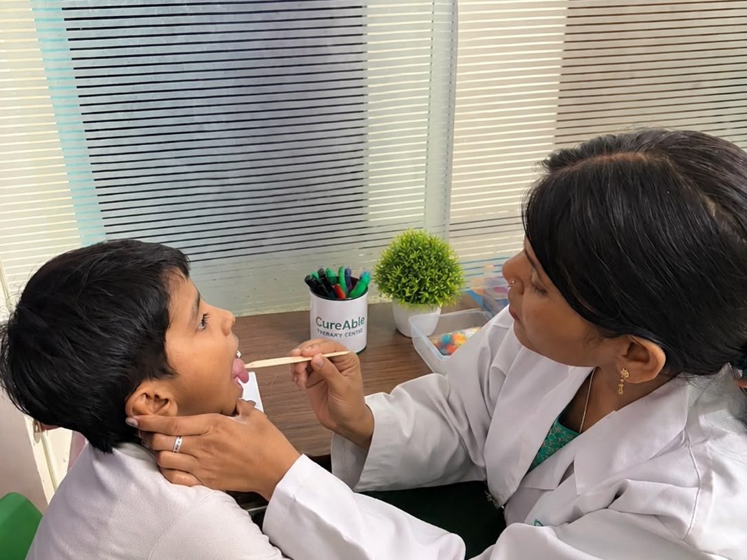 A speech therapist guiding a child's mouth movements beside a window at the Dwarka Centre.